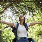 Mujer disfrutando de la naturaleza con los brazos abiertos, símbolo de salud mental y conexión con el planeta